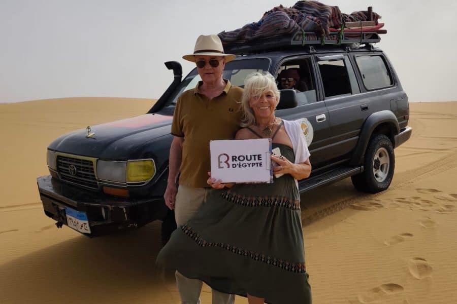 Voyage en 4x4 dans le désert égyptien avec deux touristes devant un véhicule.
